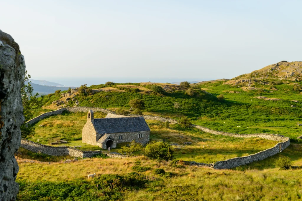 The oval churchyard enclosure of Llangelynnin Old Church seen from Craig Celynin, with Llandudno and the Irish Sea just visible beyond.