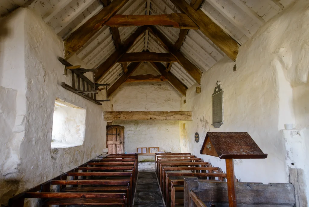 The nave interior looking west. Wooden pews, flagstone floor, and a coffin bier mounted on the south wall. Natural light only.