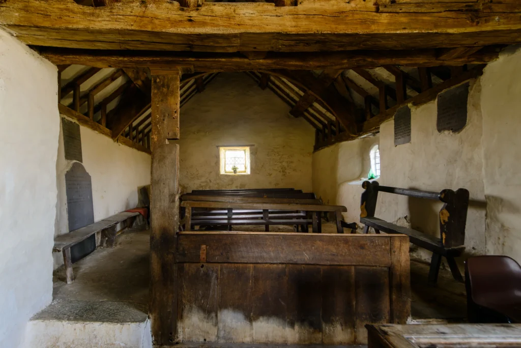The men's chapel interior, looking north. Stone walls, simple wooden seating, and natural light through a small east window.