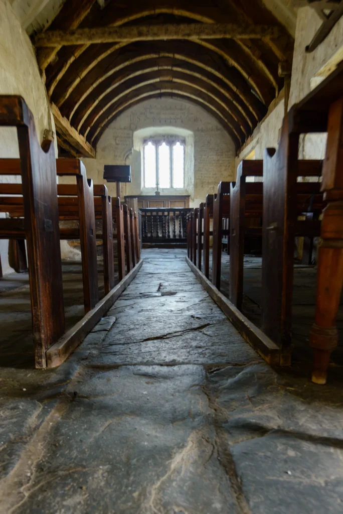 The nave floor looking east toward the altar. Ancient flagstones, worn smooth, with oak pews on either side.