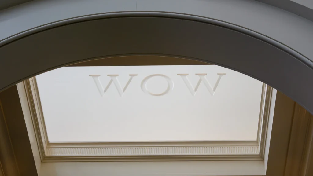 Ornate plaster archway framing a recessed skylight with 'WOW' lettering embossed into the panel, photographed from below.