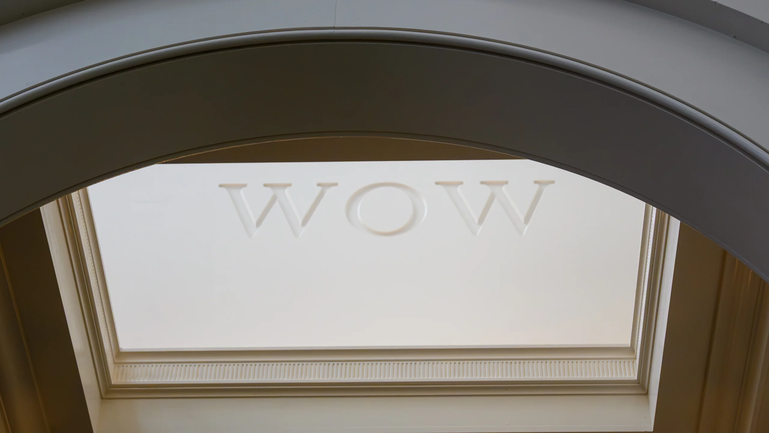 Ornate plaster archway framing a recessed skylight with 'WOW' lettering embossed into the panel, photographed from below.